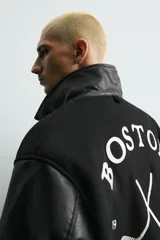 Cazadora estilo varsity con cuerpo de tejido con lana y mangas de efecto piel. Presenta cuello solapa, cierre frontal con botones a presión, bolsillos laterales y puños con elástico a rayas. Incluye parches y bordados decorativos en el frente.