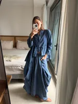 Pollera larga de jean fino color azul, con diseño amplio, elástico en la cintura y bolsillos delanteros grandes. Cuenta con pinzas y superposiciones de tela en los laterales que aportan volumen y movimiento.