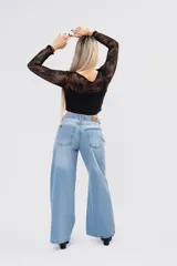 Blusa de encaje floral blanco con transparencias, mangas largas, escote cruzado y lazos frontales con volados.