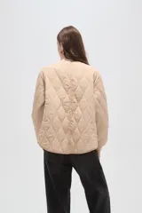 Campera acolchada de poliamida en color beige, con diseño de costuras en rombos, cuello alto, cierre frontal y bolsillos delanteros con solapa.
