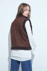 Chaleco de gamuza marrón con interior de corderito sintético, diseño sin mangas con terminaciones de corderito y detalle de tachas metálicas doradas en el frente.