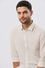 Camisa de lino a rayas finas en tonos beige y blanco, de manga larga con puños vueltos, cuello camisero y cierre frontal de botones. Cuenta con un pequeño logo bordado en el pecho.