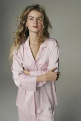 Pijama de dos piezas en tejido fluido de satén color rosado con ribetes en color contrastante. Camisa de manga larga con cuello abierto, botones adelante y bolsillo superior abierto, junto con un pantalón de pierna amplia.
