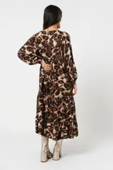 Vestido midi de corte holgado con estampado animal print en tonos marrones y beige. Tiene cuello redondo con lazo, mangas largas abullonadas y falda amplia con volantes. Incluye cinturón marrón con tachas.