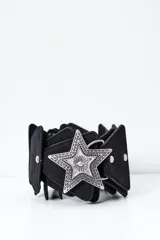 Cinto negro de diseño ancho con múltiples piezas superpuestas y una gran hebilla metálica plateada en forma de estrella con grabados texturizados.