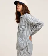 Camisa de jean de manga larga con diseño de rayas verticales, cuello inglés, cierre frontal con botones y dos bolsillos grandes en el frente.