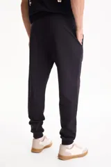 Pantalón de jogging negro sin friza, con puños elastizados en los tobillos y cordón ajustable en la cintura.