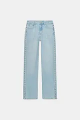 Jeans de tiro medio con cinco bolsillos, pernera recta y diseño de tachas laterales con bajo con abertura. Cuenta con cierre frontal con cremallera y botón.