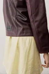 Chaqueta de cuero negra con cuello redondo, cierre frontal de botones forrados y bolsillos ribeteados con detalles de costura decorativa.