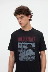Remera negra de algodón pesado con calce relaxed, cuello redondo y manga corta. Cuenta con un diseño gráfico central que combina fotografía de un cactus en tonos grises con la leyenda "Wilder Days" en granate.