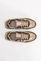 Zapatilla acordonada de estilo urbano, combinando tonos beige y marrón, con paneles superpuestos y suela de plataforma dentada.