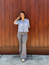 Camisa de corte recto y calce holgado, confeccionada en tela liviana color celeste con estampado de rayas verticales blancas con detalles de hojas. Presenta cuello en V, cierre frontal con botones de madera y mangas tres cuartos con terminación elástica.