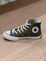 Zapatillas de lona verde militar de caña alta, con cordones blancos y puntera de goma blanca. Logo de durazno engomado en la base y en la cara interna.