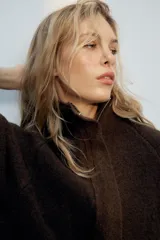 Chaqueta de punto marrón de textura bouclé, con cuello subido, manga larga ancha y cierre frontal oculto con cremallera.