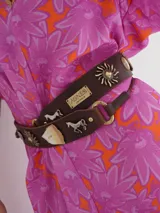 Cinturón negro con apliques de caballos plateados y argollas doradas. Se ajusta con un lazo en la parte posterior.