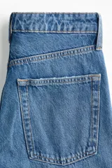 Jean de tiro alto con corte wide leg y diseño de cinco bolsillos. Presenta un acabado en denim azul con detalles de roturas desgastadas en la parte frontal.