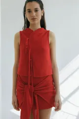 Top sin mangas de tejido punto arroz color rojo vibrante, con cuello mao y detalle de lazos finos cruzados en el frente.