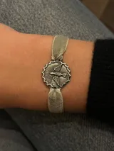 Pulsera con cinta de terciopelo color gris claro y dije plateado con la imagen del Espíritu Santo.