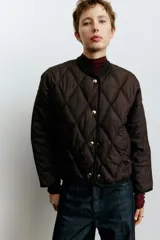 Campera de tejido guateado con diseño de rombos, cuello redondo acanalado, cierre frontal con botones a presión y bolsillos laterales. Presenta ribetes en los bordes y forro interior.