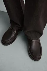 Zapato tipo náutico de piel marrón con acabado abatanado, pas Cordones del mismo tono, ojetes metálicos, plantilla de piel y suela track de goma.