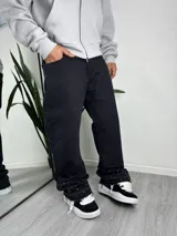Jeans de denim negro con diseño acampanado y detalles de tachas aplicadas en los botamangas, que presentan terminación deshilachada.