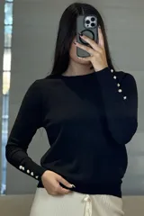 Buzo de hilo negro con cuello redondo, manga larga y detalle de botones decorativos en los puños y a lo largo del antebrazo.
