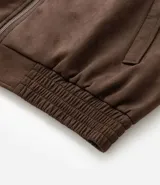 Campera masculina de estilo casual con cuello inglés, cierre frontal por cremallera, bolsillos laterales y ajuste elástico en el bajo. Presenta detalles de recortes en la parte superior delantera.