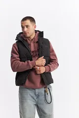 Chaleco puffer acolchado color azul marino, con capucha fija, cierre frontal con solapa de botones a presión y bolsillos laterales con cierre. Presenta un parche con el logo de la marca en el pecho.