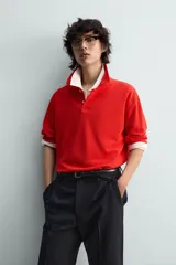 Polo de manga larga color rojo, confeccionado en tejido de algodón con estructura piqué, cuello solapa y cierre frontal de botonadura. Presenta aberturas laterales en el bajo.