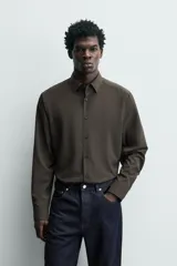 Camisa slim fit de color marrón oscuro, con cuello italiano, manga larga con puños abotonados y cierre frontal de botones. Confeccionada en tejido de fácil cuidado que minimiza la necesidad de planchado.