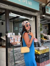 Bandolera pequeña de diseño rectangular en color beige, confeccionada en cuero sintético. Presenta una correa larga ajustable del mismo material y cierre superior con cremallera. Incluye el logo de la marca grabado en la parte frontal.