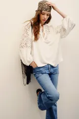 Camisa blanca de manga larga con detalles de encaje guipure en el pecho y las mangas, cuello en V y corte holgado.