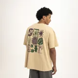 Remera color beige de corte holgado con estampado pequeño en el pecho de una flor y la letra S.