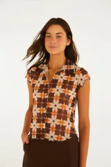 Top de manga corta con cuello camisero y cierre frontal de botones, confeccionado en tejido liviano con estampado geométrico de flores en tonos marrón, naranja y beige.