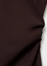 Vestido midi de color marrón oscuro, con cuello redondo, manga larga y diseño evasé. Presenta un detalle drapeado en la cintura y cierre de cremallera en la parte posterior.