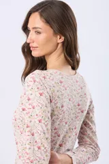 Remera de manga larga con estampado floral sobre base beige, confeccionada en tejido de algodón. Presenta cuello redondo con una pequeña abertura frontal cerrada por una hilera de botones.