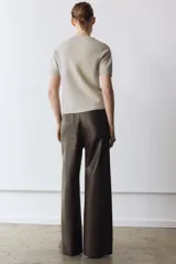Pantalón de tiro alto confeccionado en tejido efecto piel, con diseño de pierna ancha y costuras marcadas en el delantero. Presenta cintura con trabillas, cierre frontal con cremallera, botón y gancho metálico, y bolsillos de plastrón en la espalda.