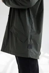 Campera impermeable verde con capucha, cierre frontal con botones a presión y bolsillos laterales con solapa.