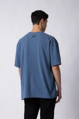Remera de corte oversized en color marrón, confeccionada en tejido de algodón con textura de micropanal. Presenta cuello redondo con detalle de costura en forma de X y mangas cortas de estilo caído.