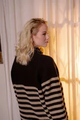 Sweater de punto en color crema con rayas horizontales en tono dorado. Presenta un diseño de cuello redondo con una solapa lateral decorada con botones metálicos dorados y corte holgado.