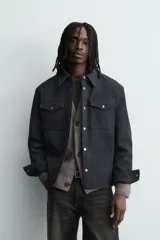 Sobrecamisa de corte relajado confeccionada en tejido efecto piel color marrón oscuro. Presenta cuello solapa, cierre frontal con botones metálicos, mangas largas con puños abotonados y dos bolsillos de plastrón con solapa en el pecho.