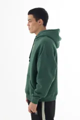 Buzo hoodie verde oscuro con estampa serigráfica frontal de alta definición con una escena urbana en estilo puntillista y logo VERNAL con efecto dorado envejecido. Corte oversize con hombros caídos, capucha doble y bolsillo canguro.