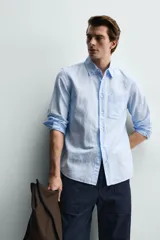 Camisa regular fit de manga larga con diseño a rayas verticales celestes y blancas. Cuenta con cuello abotonado, bolsillo de parche en el pecho y cierre frontal con botones.