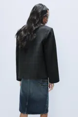 Blazer corto de corte oversize con estampado de cuadros, cuello con solapa de muesca, manga larga y cierre frontal cruzado con un botón. Cuenta con bolsillos decorativos de vivo en el frente y forro interior.