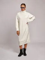 Vestido midi de punto con cuello alto tipo poleron, de corte holgado y mangas largas con puños acanalados. Presenta un diseño en color blanco con sutiles motas de colores.