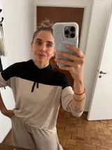 Sudadera con capucha de manga larga, color beige, con canesú negro en la parte superior de los hombros y capucha negra. Presenta cordones negros para ajustar la capucha.