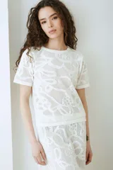Remera de manga corta tejida a máquina con patrón calado y cuello redondo.
