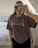 Remera marrón oversize con diseño gráfico estampado en la espalda que incluye la inscripción "Kaboa" y fechas de gira mundial.