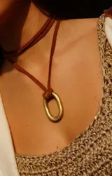 Collar tipo choker con cordón de cuero marrón trenzado y dije colgante de metal dorado con forma de óvalo alargado.