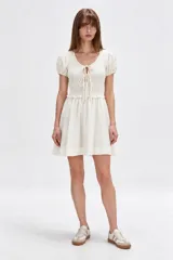 Vestido corto blanco de viscosa con mangas cortas abullonadas, cuerpo con punto smock y tiras para anudar en el escote en V, y falda evasé.